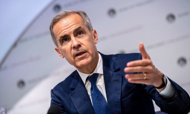 A man in a dark blue suit leans in, with his hand motioning downward, as he delivers remarks.