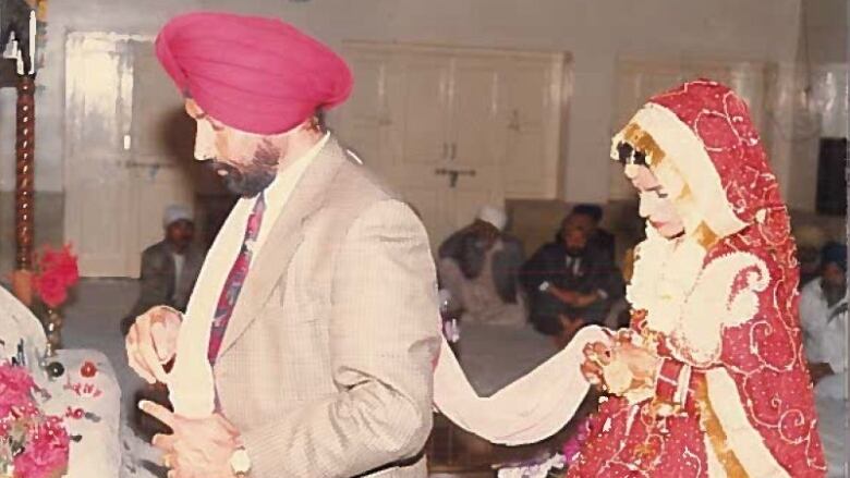 An old photo of a Sikh wedding shows a man in a turban walking with a woman holding fabric following behind him.