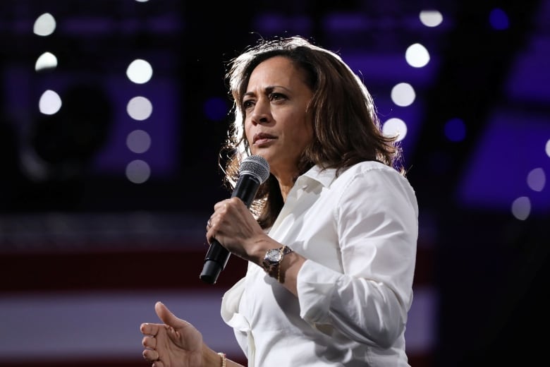 A woman in a white suit speaks into a microphone.