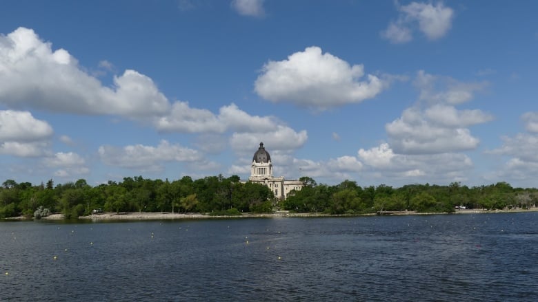 An official looking building surrounded by trees sits in the background, with a lake in front of it.