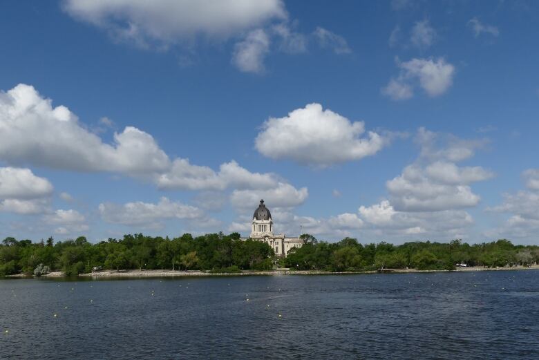 An official looking building surrounded by trees sits in the background, with a lake in front of it.