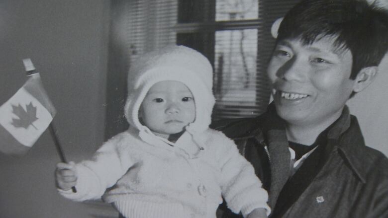 A baby holds a Canadian flag, and her father holds her.