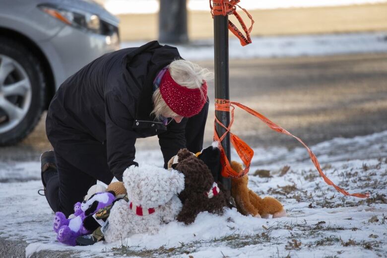 Woman kneels near stuffed animals and police tape.