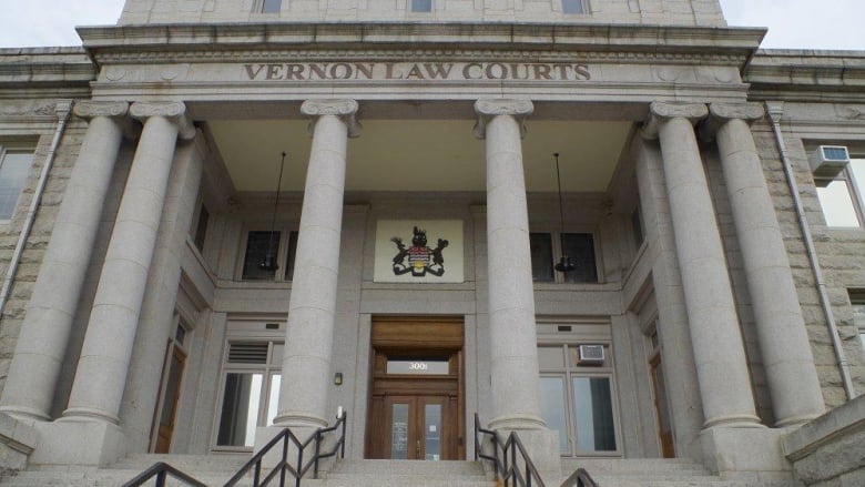 A photo of the front steps of a white stone building with a large entranceway framed by six large Roman columns with the words Vernon Law Courts in gold over the top. 