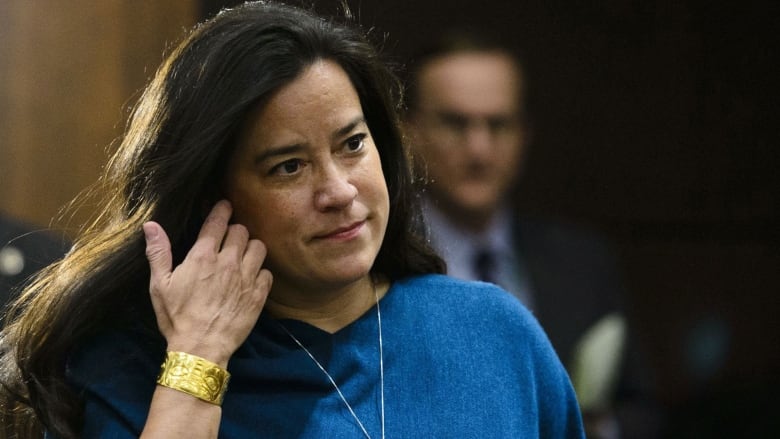 A woman in a blue sweater walks into a meeting.