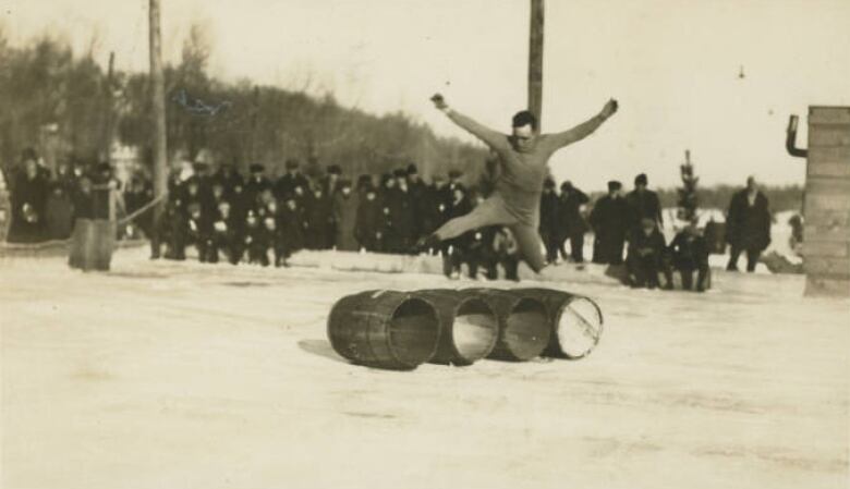 Black and white photo of a skater jumping a row of four barrels during a carnival in 1924.