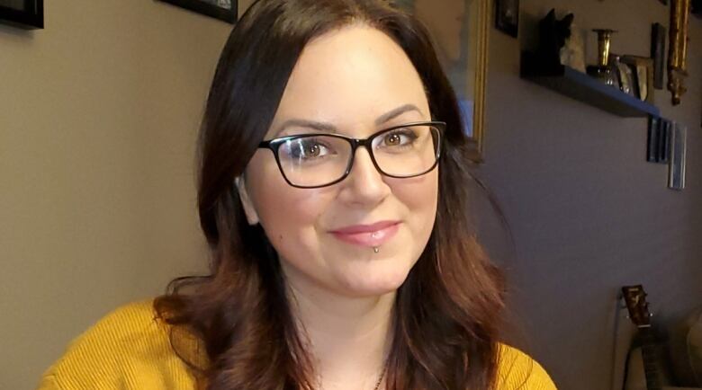 A woman wearing glasses holds a green mug and smiles at the camera.