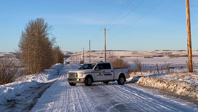 A police truck blocks a snow covered rural road. 