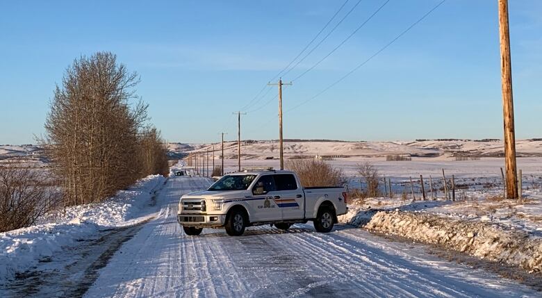 A police truck blocks a snow covered rural road. 