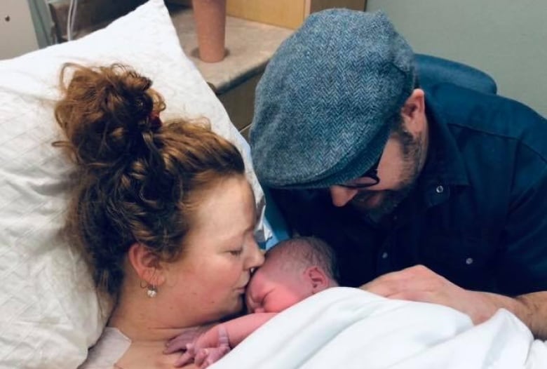 A woman kisses a newborn baby on her chest while a man looks on smiling