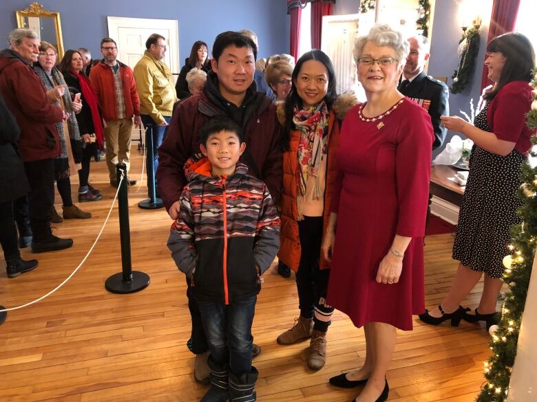 Woman in red dress smiles at the camera with a family of three at her side, as a lineup of other people wait to greet her in the background. 