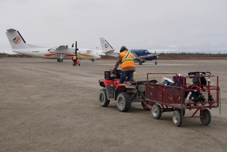 An ATV pulls a cart full of baggage across a runway toward two airplanes