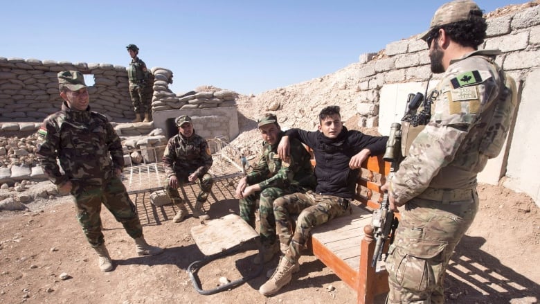 Soldiers stand in a circle next to a mud wall.