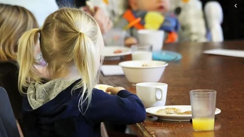 Two children sit at a table eaiting food. 