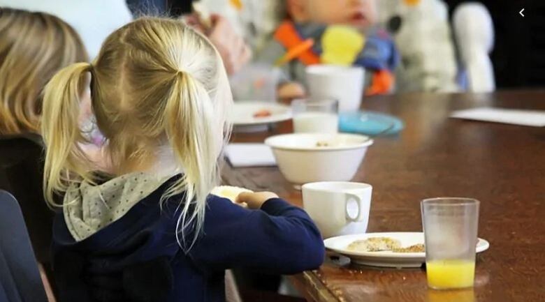 Two children sit at a table eaiting food. 