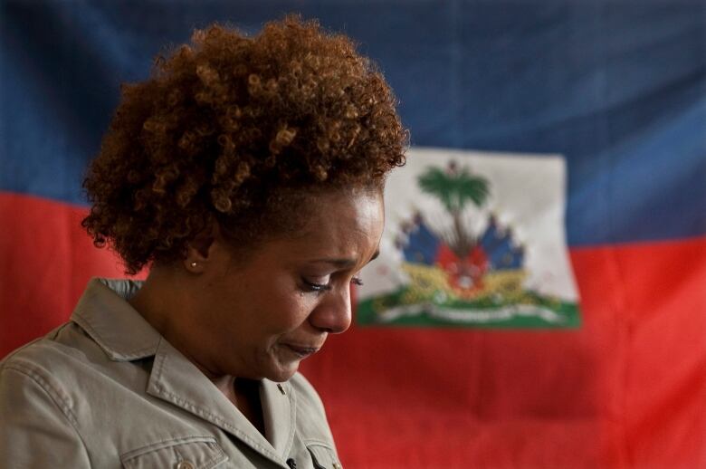 Woman with a sad expression on her face and standing in front of the flag of Haiti looks down