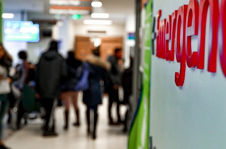 A hospital emergency department sign with several people lined up in the background, out of focus.