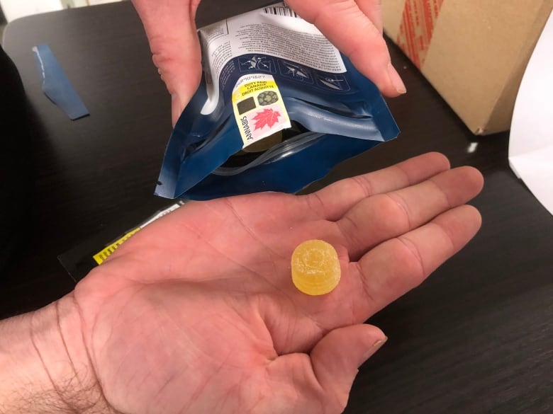 The palm of a hand holding a cannabis gummy candy next to a pouch with a warning label.