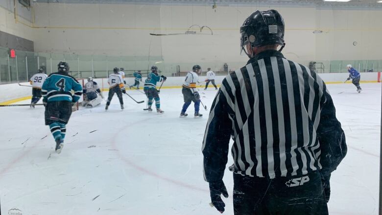 A referee watches hockey players on the ice.