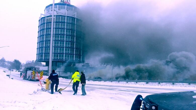 The 9-story circular building with smoke billowing up from it's right side reaching all the way to the top of the building. 