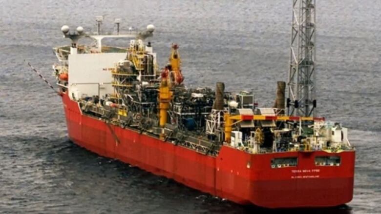 A white and red boat in the water. The deck is covered in mechanical equipment.