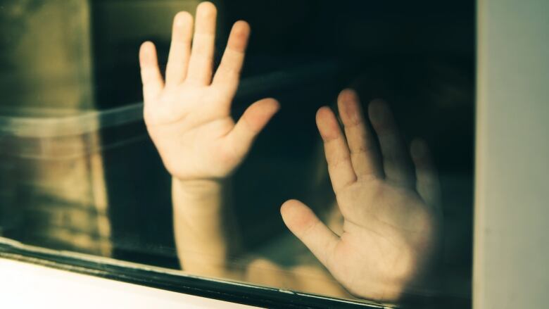 A child's hands are seen pressed up against a window.