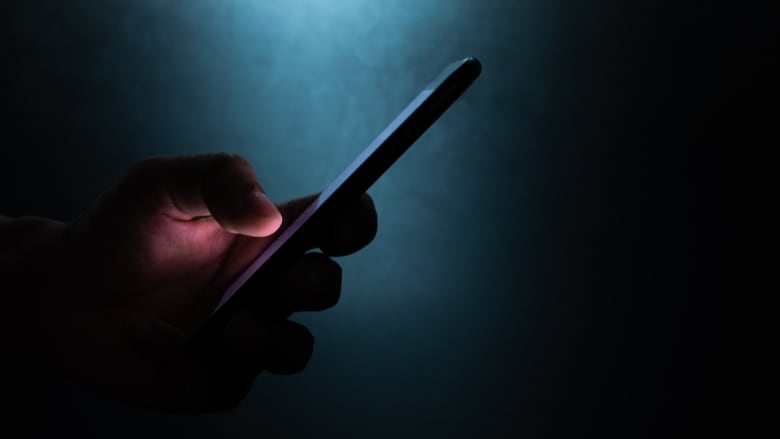 A person's hand is seen holding a mobile device in the dark.