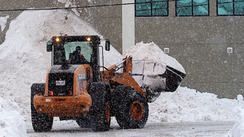 A tractor picking up a large scoop of snow. 