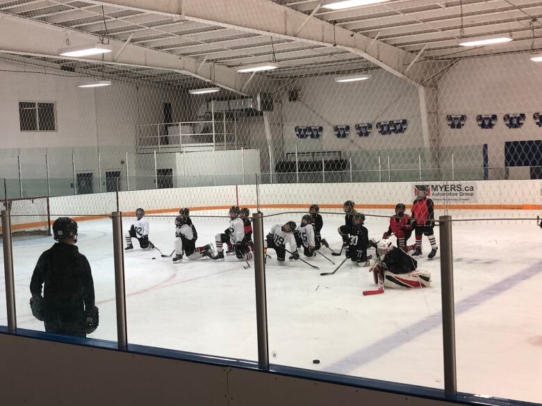 Young hockey players take a knee during a break in a practice.