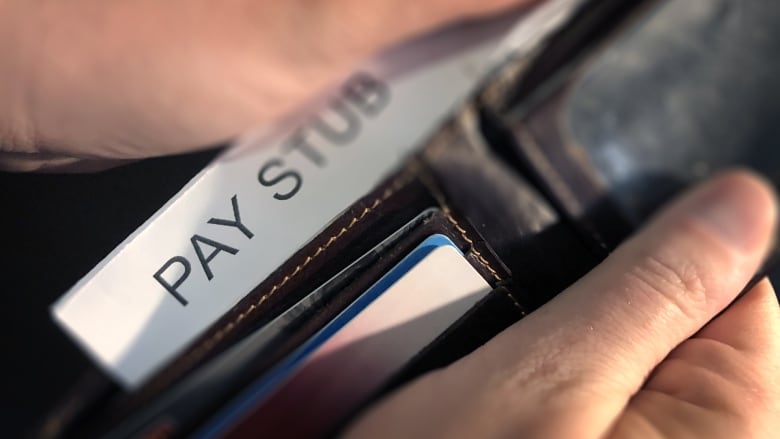 Hands hold a wallet and pull out a piece of paper that reads 'pay stub'