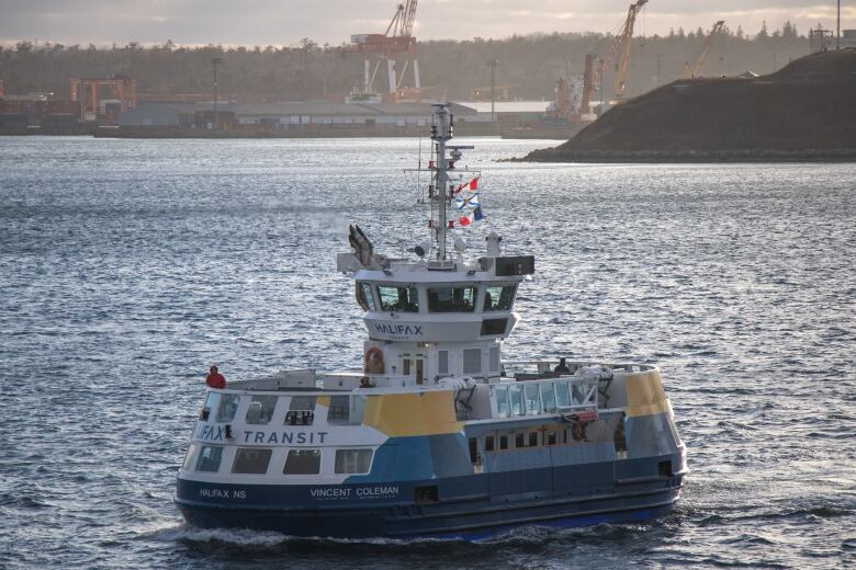 A blue and yellow Halifax Transit ferry crosses the Halifax harbour on a sunny day.