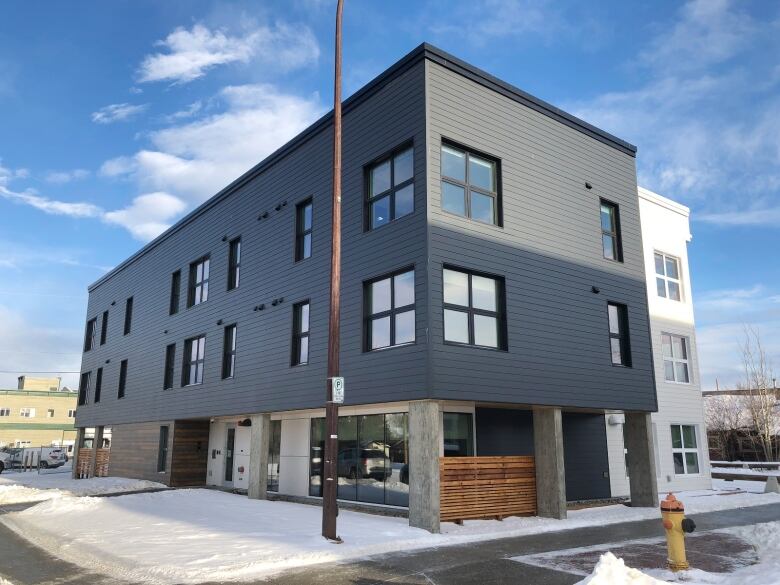 A rectangular grey 3-storey building sits on a corner lot, on a snowy day.