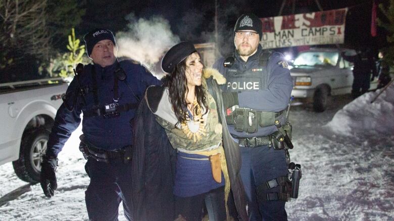 A woman is handcuffed and removed by police against a snowy background.