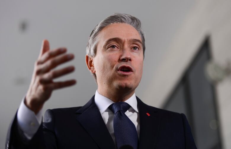 A gray-haired man in a suit speaks and gestures with his hand.