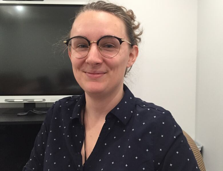 A woman wearing glasses and a navy blue blouse smiles into the camera.