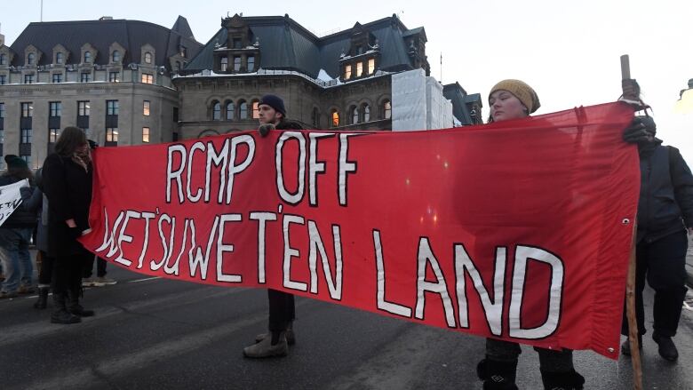 Protesters hold a big red banner reading, 