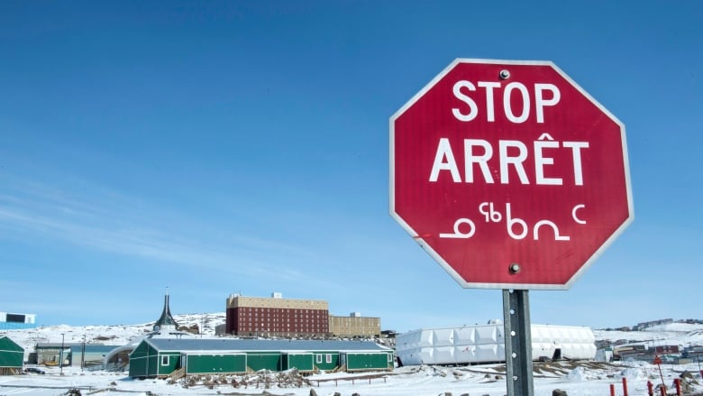 A stop sign, with English, French and Inuit syllabics, in a snowy Arctic community.