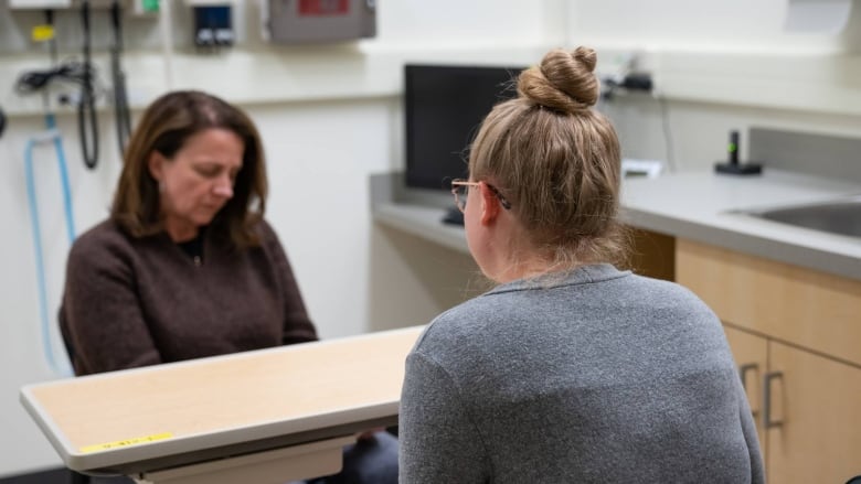 Two women sit across from one another in a medical examination office. 