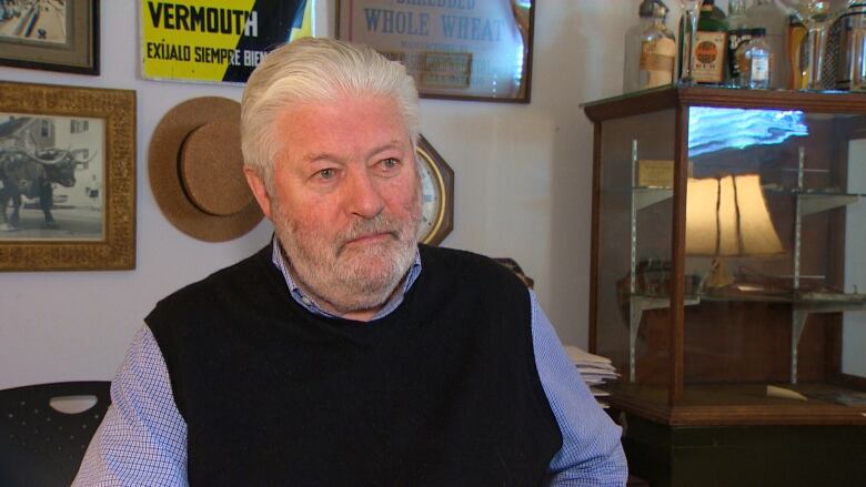 A man with white hair wearing a black vest. 