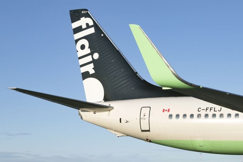 The tail of a plane with the words Flair as it flies in a blue sky.