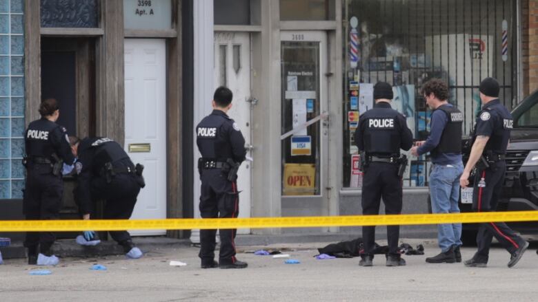 Several police officers standing behind yellow tape at a crime scene.