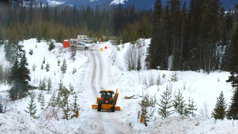 A yellow piece of heavy equipment moves along a road through forest and snow towards work trucks in the distance in this file photo from 2020. 