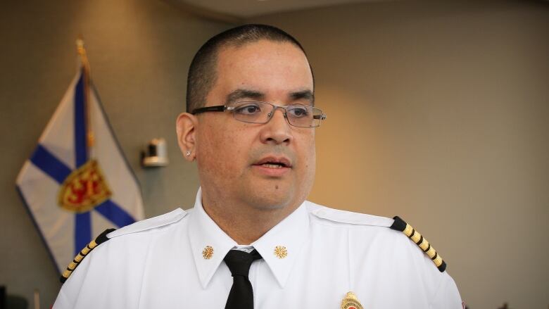 A man with glasses and a white uniform shirt speaks with a Nova Scotia flag in the background.