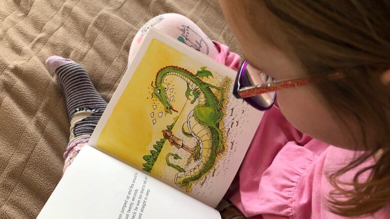 Looking over shoulder of child sitting cross-legged reading a book. An illustration shows a dragon and a young princess wearing a paper bag.