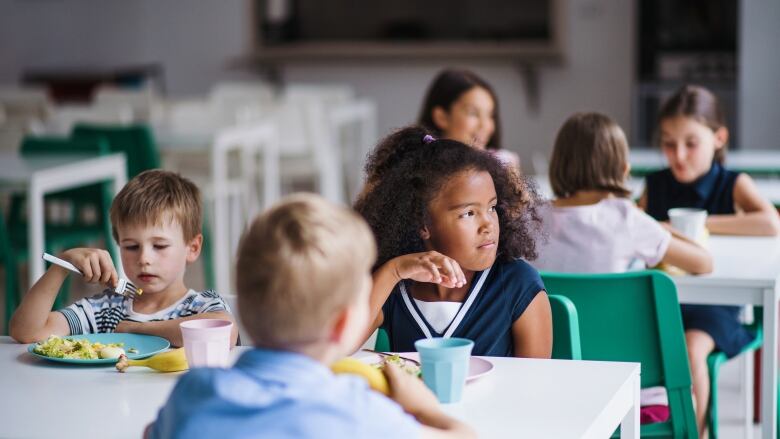 Six elementary school-aged kids sit at two tables eating. 