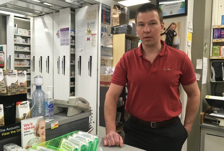 A man stands behind a counter while medical sheets line the walls in the background. 