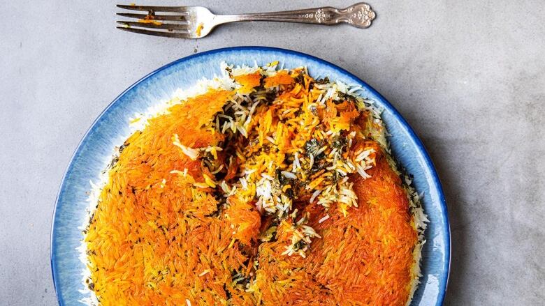 Overhead shot of a large blue plate of Sabzi Polow (Fragrant Herbed Rice). The rice is in the shape of a circle and the top of the rice is golden brown and crispy. 