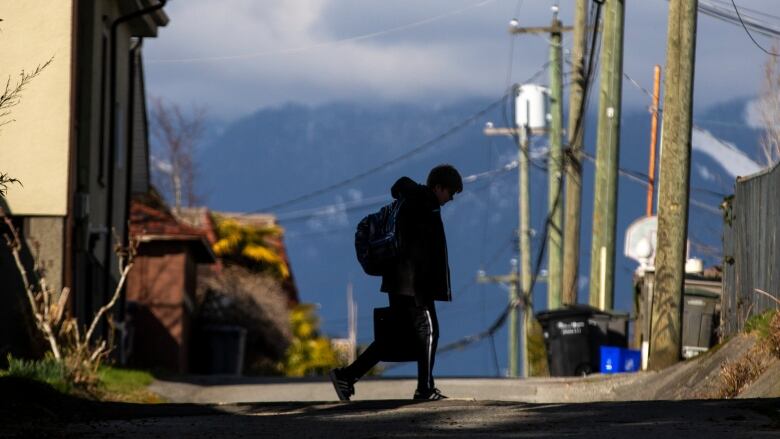 A child carrying a bag crossing a road. 