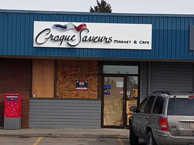 The exterior of a boarded-up shop in a strip mall with a sign that reads, 