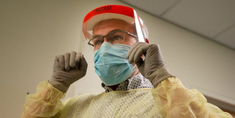 An employee at the COVID-19 screening clinic at Montreal's old Htel-Dieu Hospital illustrates how to put on protective equipment.